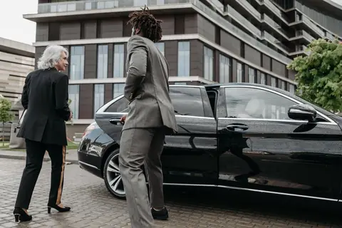Chauffeur in pak opent het portier van een zwarte Mercedes voor een klant